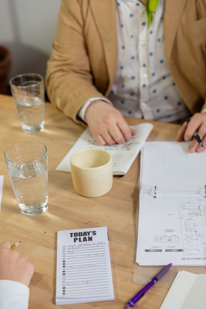 A collaborative office meeting with notebooks, coffee, and planning notes on a wooden table.